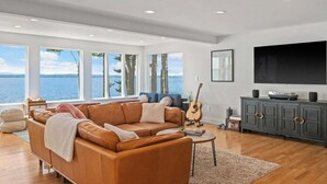 Ein Wohnzimmer mit großem Fenster, einem Ledersofa, einer Gitarre und einem Fernseher.