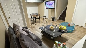 Uma sala de estar com sofá, mesa de centro com petiscos e bebidas, televisão e escada.