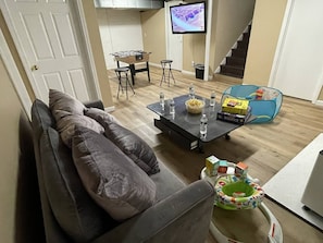 Una sala de estar con sofá, una mesita de centro con aperitivos y bebidas, televisor y una escalera.