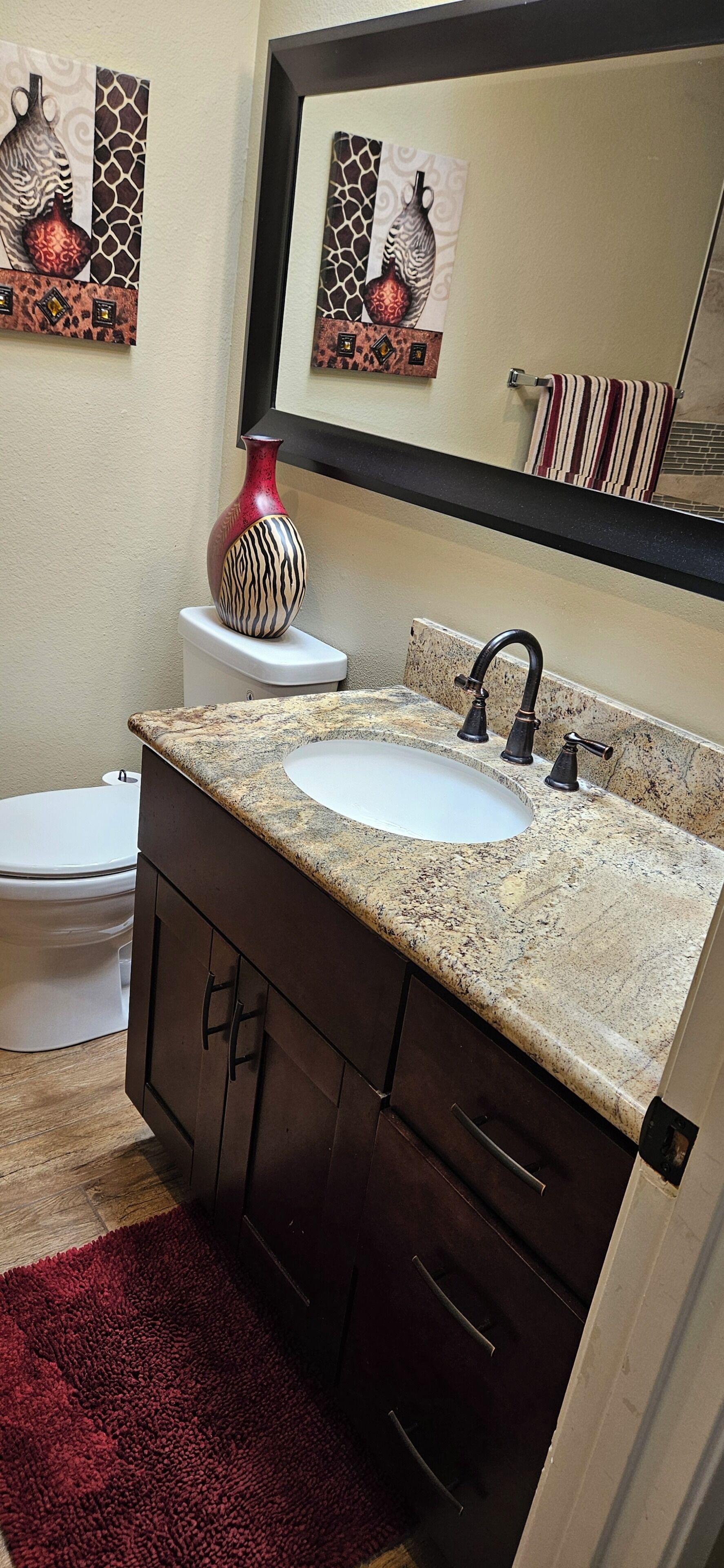 A bathroom with a granite countertop sink, dark cabinetry, a red vase, and a mirror above the sink.