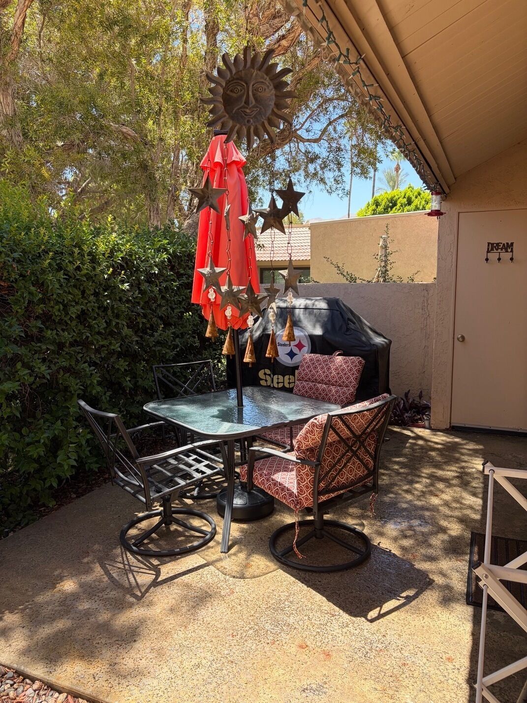 An outdoor patio with a glass table, metal chairs, a red umbrella, and a barbecue grill.