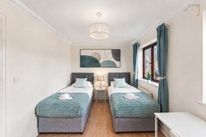 Ein Doppelzimmer mit zwei Betten, einem Nachttisch, einer Lampe, einem Fenster mit Vorhängen und einem Bild an der Wand.