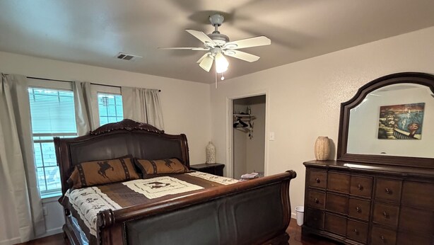 A bedroom with a wooden bed, a dresser, a ceiling fan, and a door leading to a closet.