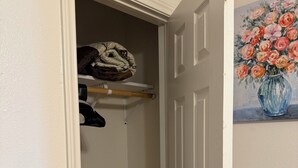 A closet with hanging clothes, a shelf with folded items, and a door with a brass doorknob.