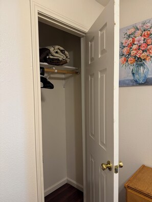 A closet with hanging clothes, a shelf with folded items, and a door with a brass doorknob. - 3-bedroom house in charming Fort Worth with AC for relaxing stays (Fort Worth)