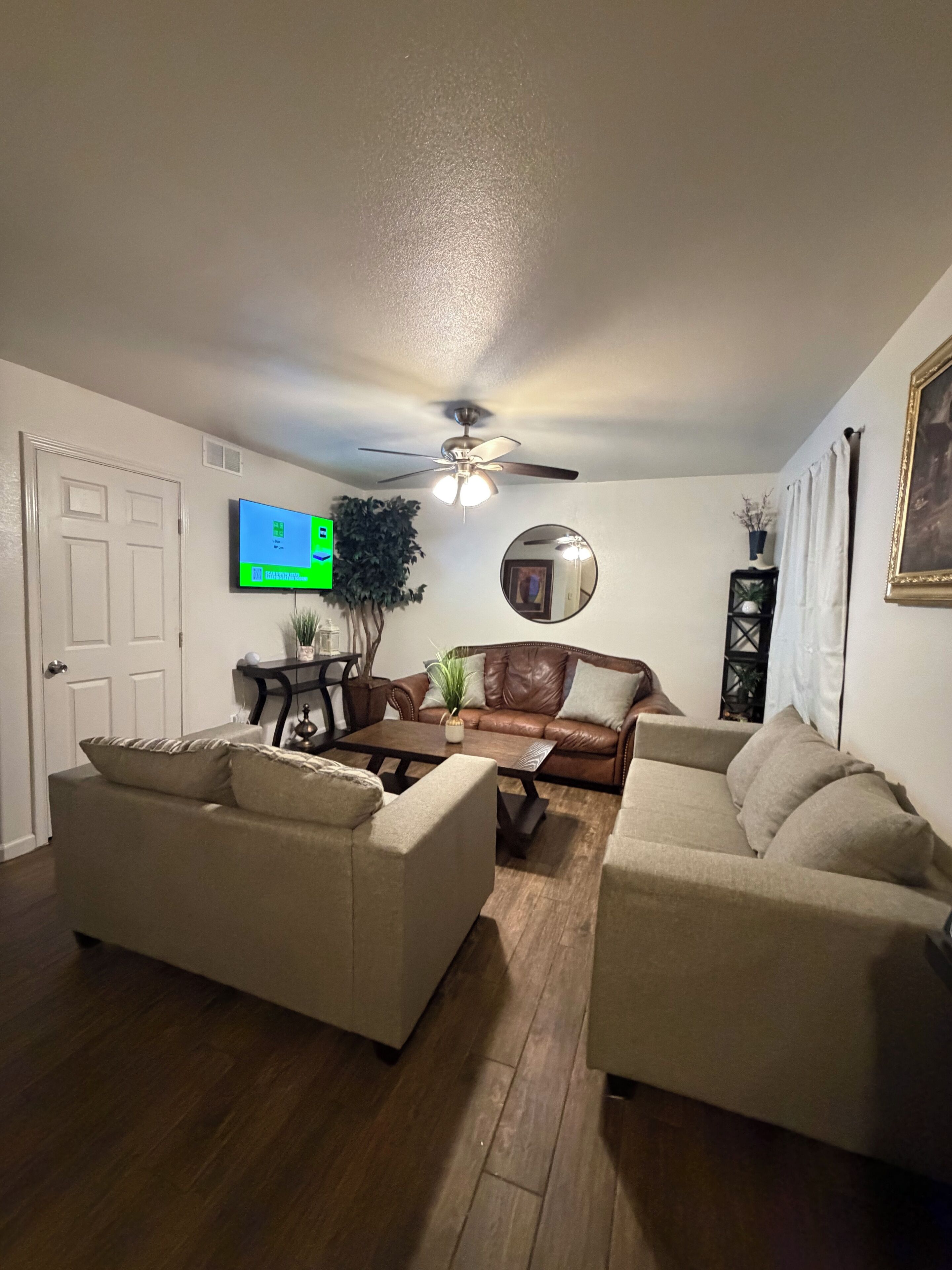 A living room with two sofas, a coffee table, a ceiling fan, a television, and a mirror.