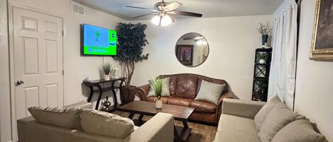 A living room with two sofas, a coffee table, a ceiling fan, a television, and a mirror.