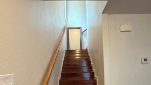 A wooden staircase with a handrail, white walls, and a light switch on the left.