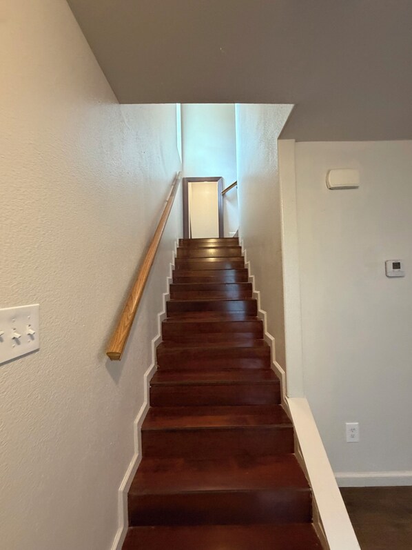 Un escalier en bois avec une rampe, des murs blancs et un interrupteur sur le côté gauche.