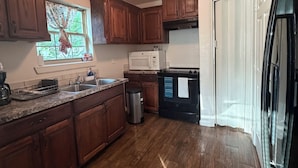 A kitchen with wooden cabinets, a microwave, a refrigerator, and a window with curtains.