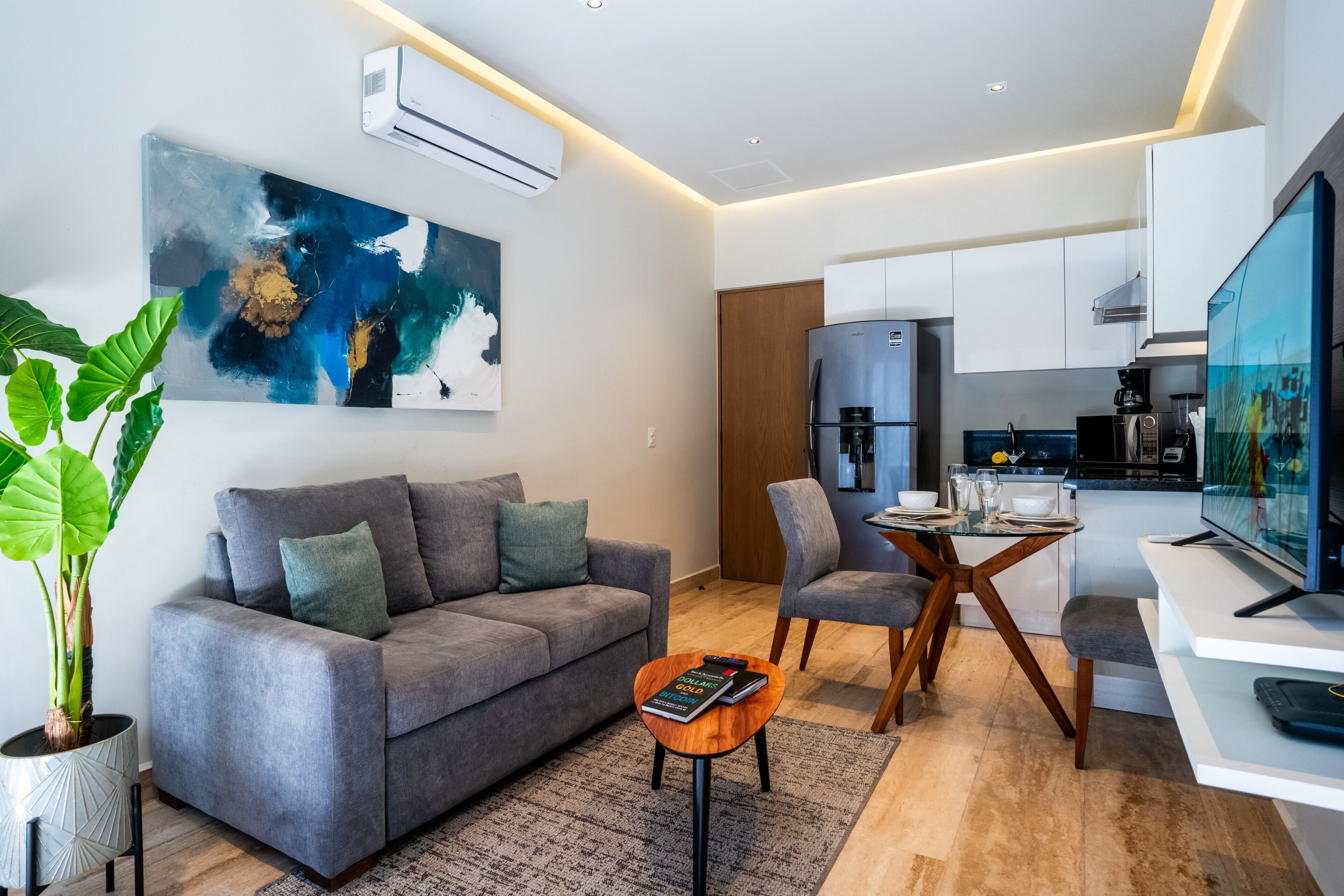 A modern living room with a grey sofa, a coffee table, and a dining area with a glass table.