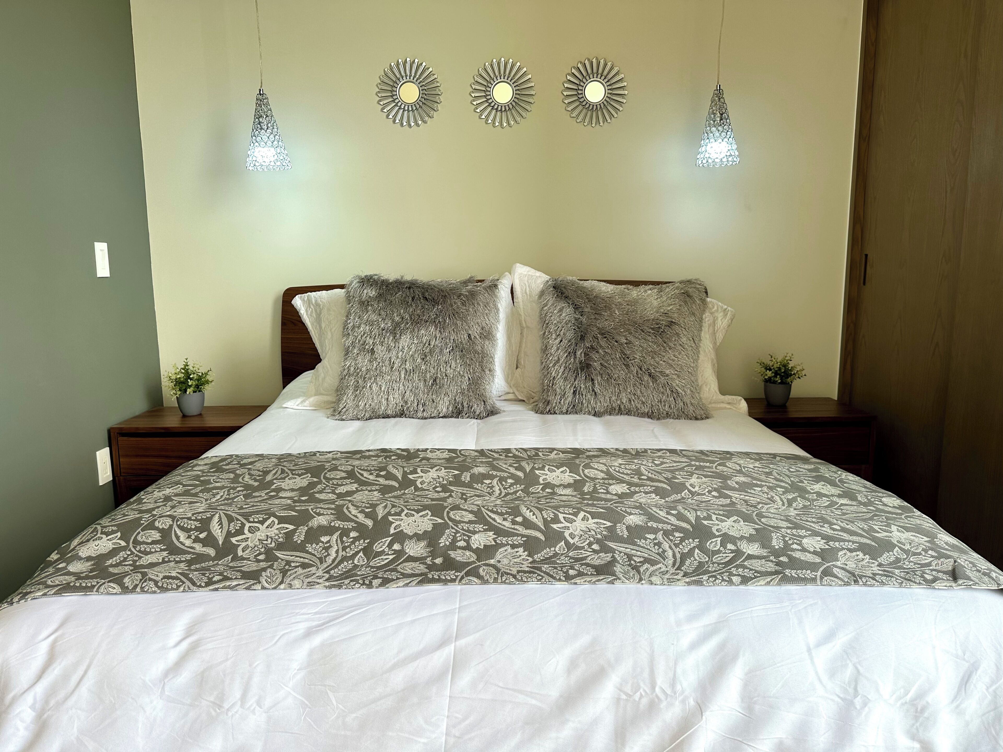A bed with a patterned bedspread, two fluffy pillows, and three wall-mounted lights.
