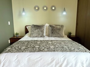 Una cama con una colcha estampada, dos almohadas mullidas y tres luces fijadas a la pared.