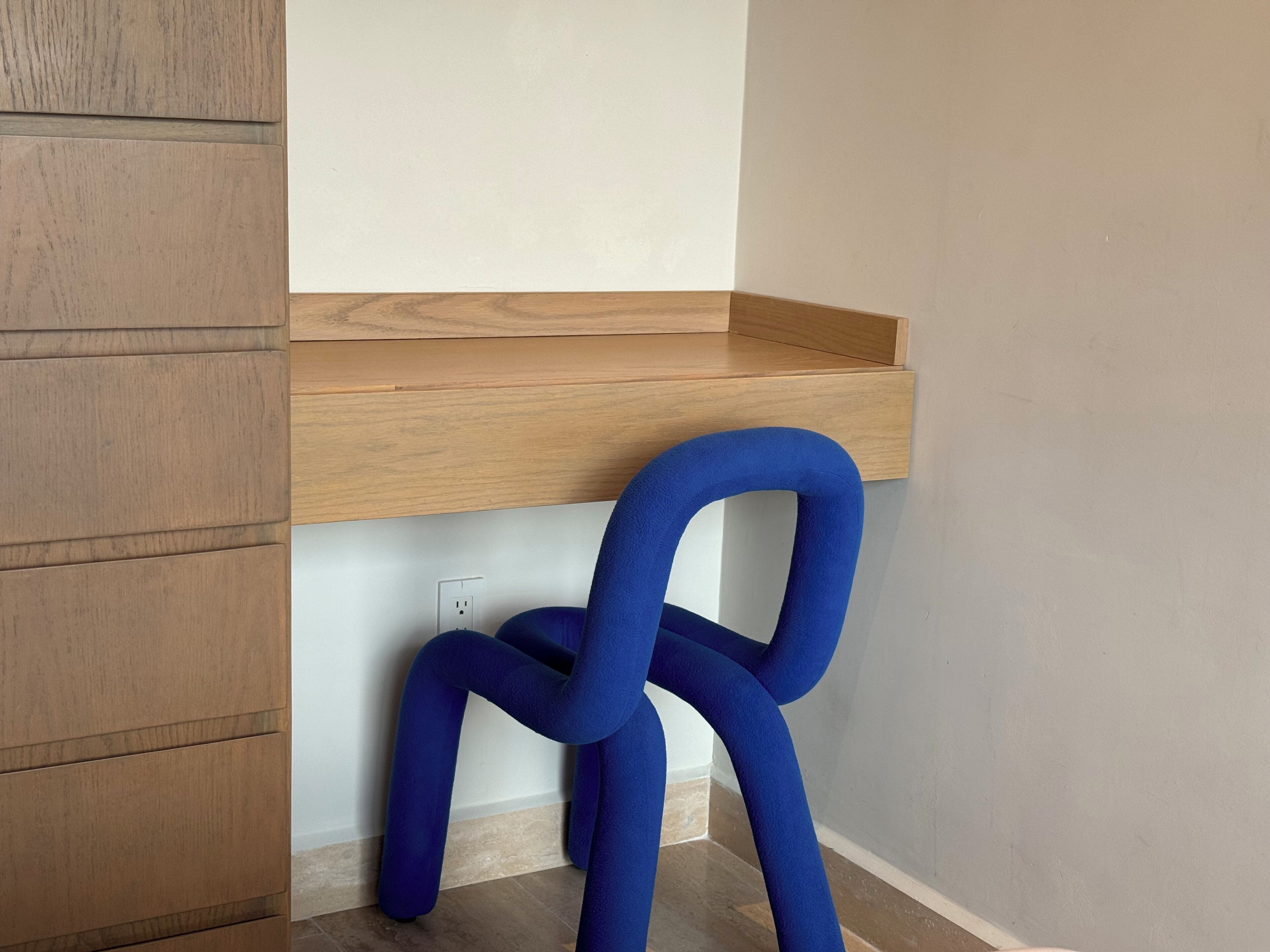 Een hoek met een houten plank, een blauwe stoel en een witte muur.