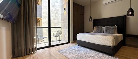 Un dormitorio con una cama grande, una puerta corrediza de vidrio a un balcón, una mesita pequeña y una lámpara colgante.