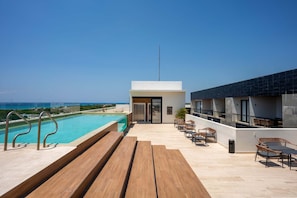A rooftop pool area with a view of the ocean, wooden benches, and outdoor seating. - Musa del Carmen (México)