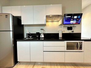 Una cocina moderna con refrigerador integrado, microondas, cafetera, licuadora y televisor de pantalla plana montado en la pared.