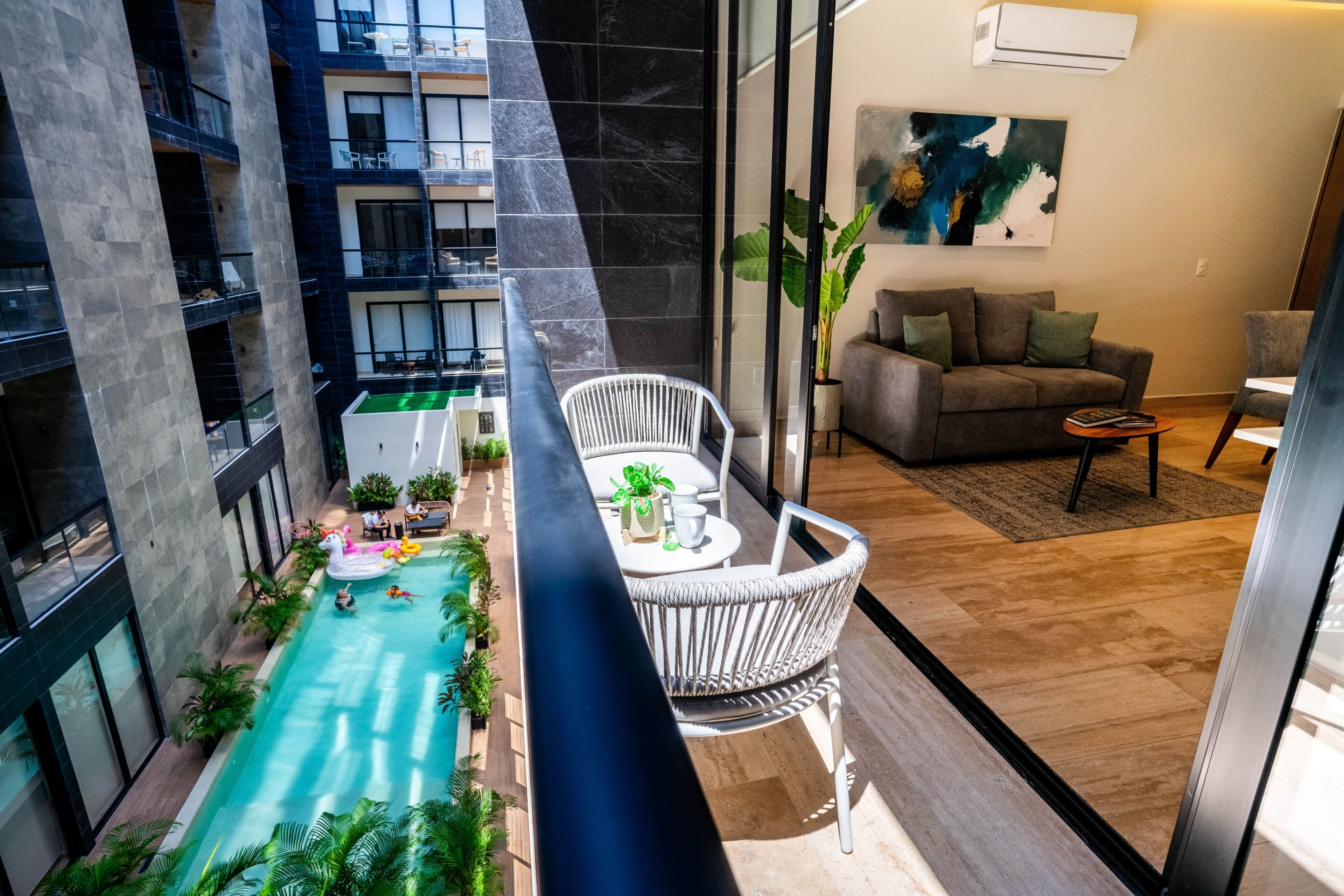 Une piscine intérieure avec vue sur un bâtiment moderne, un coin salon avec un canapé et des fauteuils, et une plante en pot.