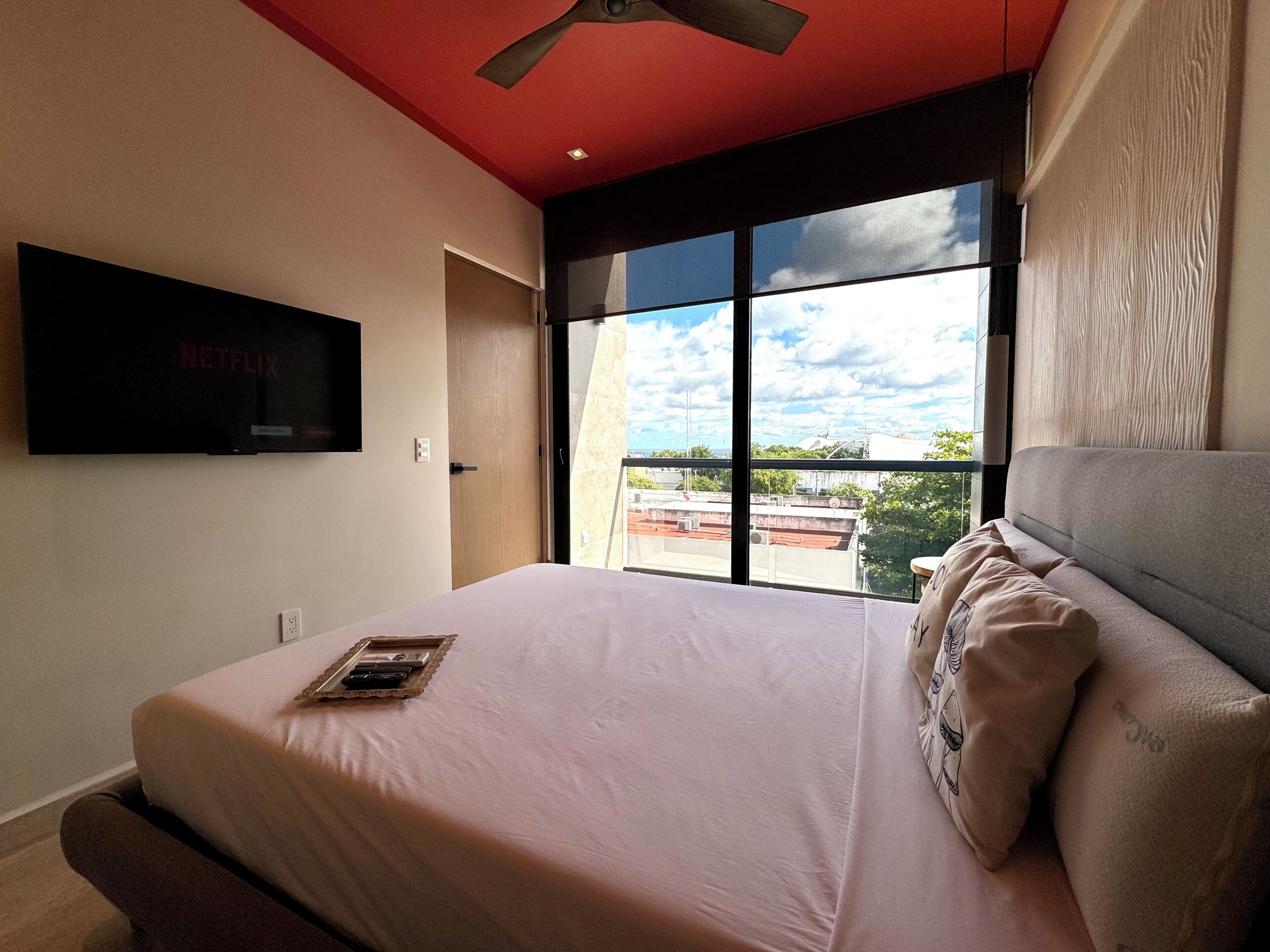 Un dormitorio con una cama, un televisor montado en la pared y un ventanal grande.