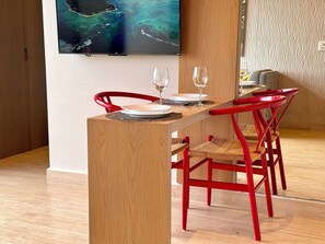 Un comedor con una mesa de madera, sillas rojas y un televisor en la pared mostrando un paisaje costero.