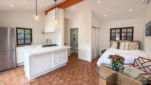 Una cocina moderna con una isla central, un comedor con mesa de vidrio y un dormitorio con cama grande y ventana.