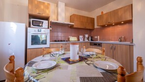 A compact kitchen with wooden cabinets, a built-in oven, a microwave, and a dining area with a table set for two. - Camillou's House (PRINSUEJOLS)