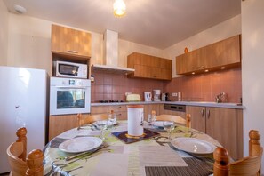 Eine kleine Küche mit Holzausstattung, einem eingebauten Ofen, einer Mikrowelle und einem Essbereich mit Tisch für zwei Personen.