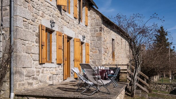 A stone building with wooden shutters, a patio with a table and chairs, and a staircase leading to a higher level. - Camillou's House (PRINSUEJOLS)