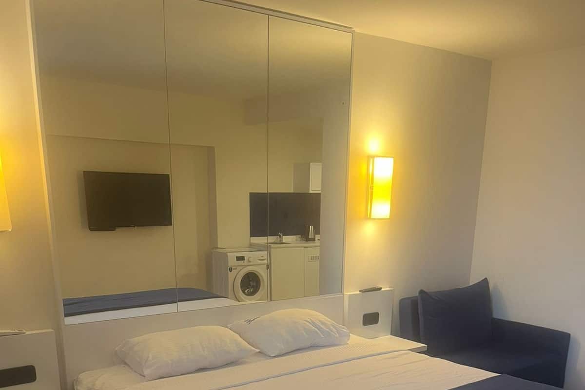 A modern hotel room with a large bed, a built-in washing machine, a flat-screen TV, and a bedside table.