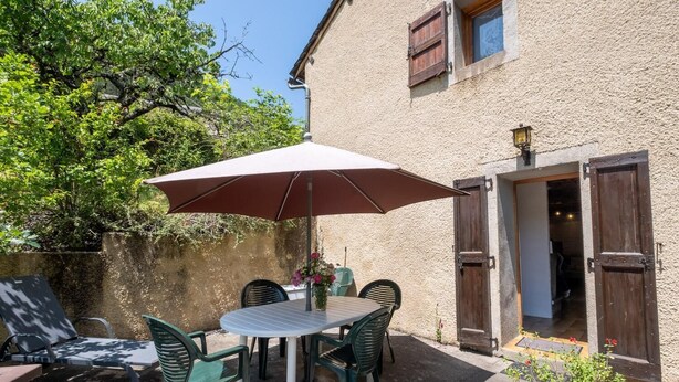 Un patio al aire libre con mesa y sillas, una sombrilla y la entrada de un edificio.