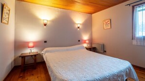 Un dormitorio con techo de madera, dos lámparas de noche, una cama con colcha blanca y una ventana con cortina.