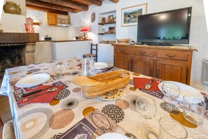 Una mesa de comedor dispuesta con platos, vasos y una cesta, en una habitación con televisor y armarios de madera.