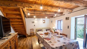 Un comedor con una mesa dispuesta para cuatro, vigas de madera en el techo y un televisor sobre un mueble de madera.