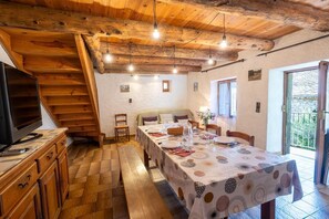 Ein Essbereich mit Tisch für vier Personen, Holzbalken an der Decke und einem Fernseher auf einer Holzkassette.