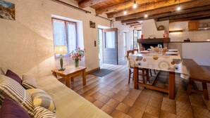 Una sala de estar acogedora con un sofá, una mesa de comedor para cuatro personas y una zona de cocina con vigas de madera y suelo de baldosas.