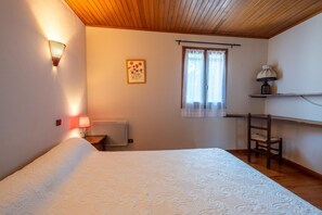 Un dormitorio con cama, mesita de noche, lámpara, ventana con cortinas, toalla y estante con lámpara.