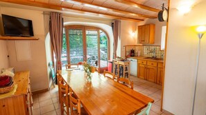 Ein Essbereich mit einem Holztisch und -stühlen, eine Küche mit Holzschränken und ein an der Wand montierter Fernseher.