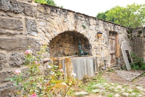 A stone building with a rustic archway, a metal sculpture, and a wooden door. - Domaine Rivière (6–7 people) (BRENOUX)
