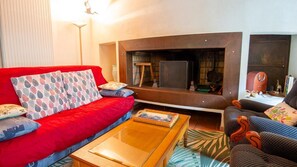 A living room with a red sofa, a wooden coffee table, and a fireplace. - Domaine Rivière (6–7 people) (BRENOUX)