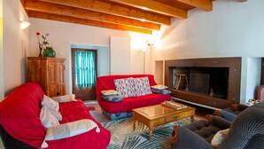 A living room with a red sofa, a wooden cabinet, a fireplace, and a large window with curtains. - Domaine Rivière (6–7 people) (BRENOUX)