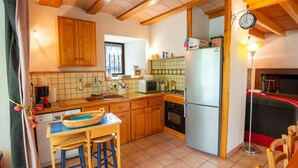 A compact kitchen with wooden cabinets, a sink, a microwave, a refrigerator, and a dining area with stools. - Domaine Rivière (6–7 people) (BRENOUX)