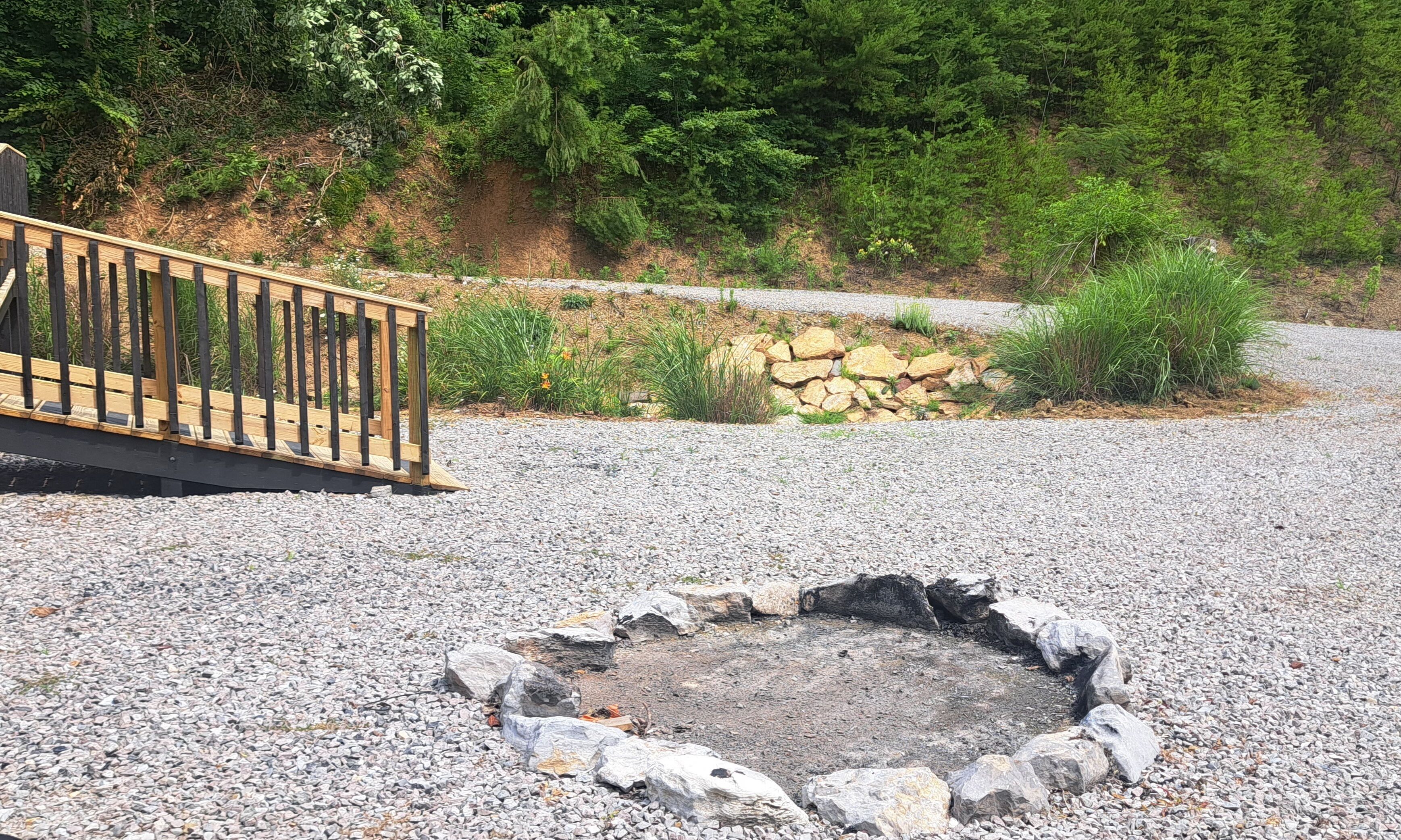 Ein Kiesbereich mit Feuerstelle, einer Holzterrasse und einer Steinmauer.