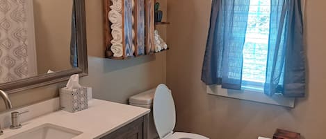 A bathroom with a sink, toilet, towel rack, and window with curtains.