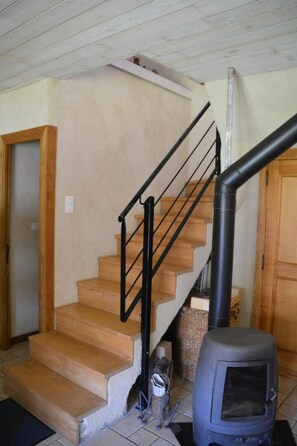 A staircase with wooden steps and black railings, leading to a room with a stove. - The Maison Caussenarde at La Bazalgette (SAINT ETIENNE DU VALDONNEZ)