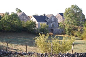 A stone building with multiple chimneys, surrounded by trees and a fenced field. - The Maison Caussenarde at La Bazalgette (SAINT ETIENNE DU VALDONNEZ)