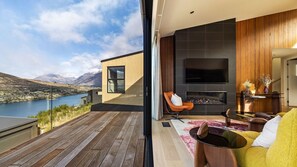 A modern interior with a fireplace, seating area, and a large window overlooking a scenic landscape. - The Middleton Escape (Queenstown)