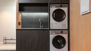 A compact laundry room with two washing machines, a sink, and a metal drying rack. - The Middleton Escape (Queenstown)