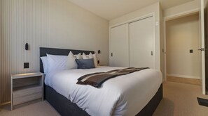 Un dormitorio con cama, mesitas de noche, armario e iluminación en la pared.
