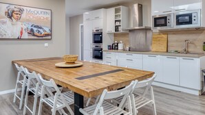Une cuisine moderne avec des meubles blancs, des appareils en acier inoxydable et une table à manger en bois, assortie de chaises blanches.
