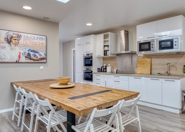 Una cocina moderna con armarios blancos, electrodomésticos de acero inoxidable y una mesa de comedor de madera con sillas blancas.